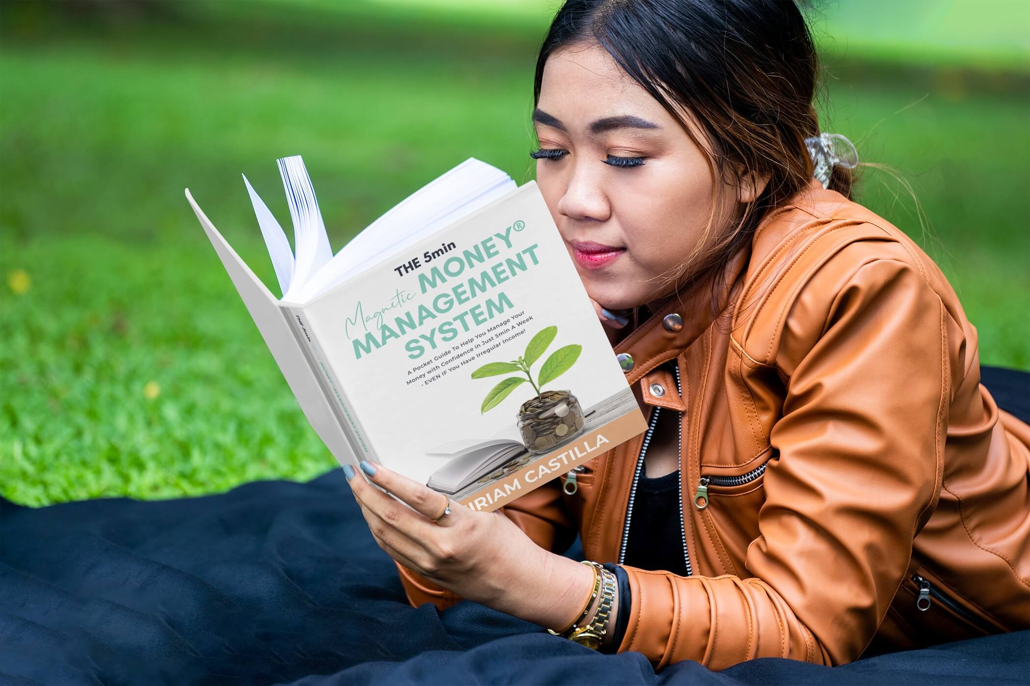 Woman lying in park reading the Magnetic Money Management System Book